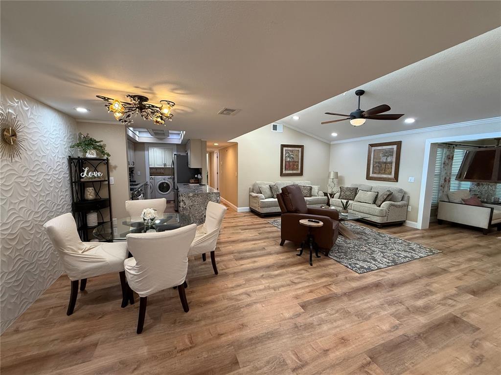 An open-concept living and dining area features wood-look flooring, a textured accent wall, and vaulted ceilings — 6861 WOODWIND DR UNIT 75, SARASOTA, FL