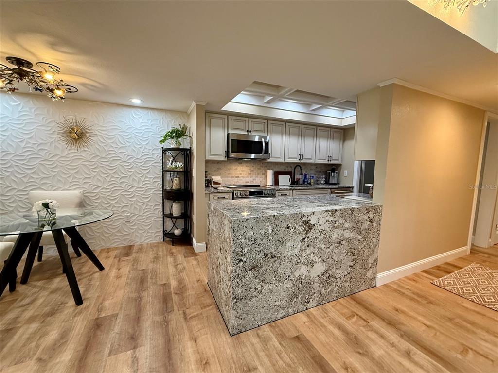 A kitchen with granite countertops and light cabinetry opens to a dining area with textured walls — 6861 WOODWIND DR UNIT 75, SARASOTA, FL