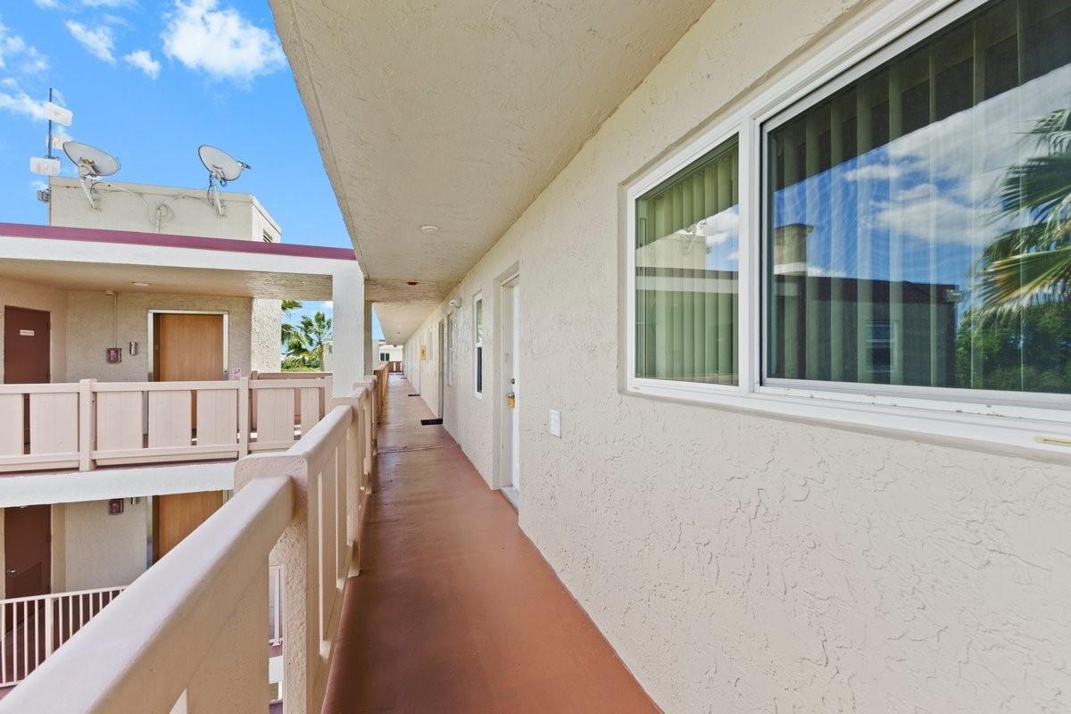 An exterior walkway with a tan stucco wall, a window, and a wooden railing — 2106 S Cypress Bend Drive # 506, Pompano Beach FL 33069, POMPANO BEACH, FL