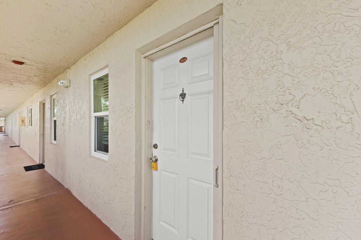 A white exterior door with a lockbox is located along a covered outdoor apartment walkway — 2106 S Cypress Bend Drive # 506, Pompano Beach FL 33069, POMPANO BEACH, FL