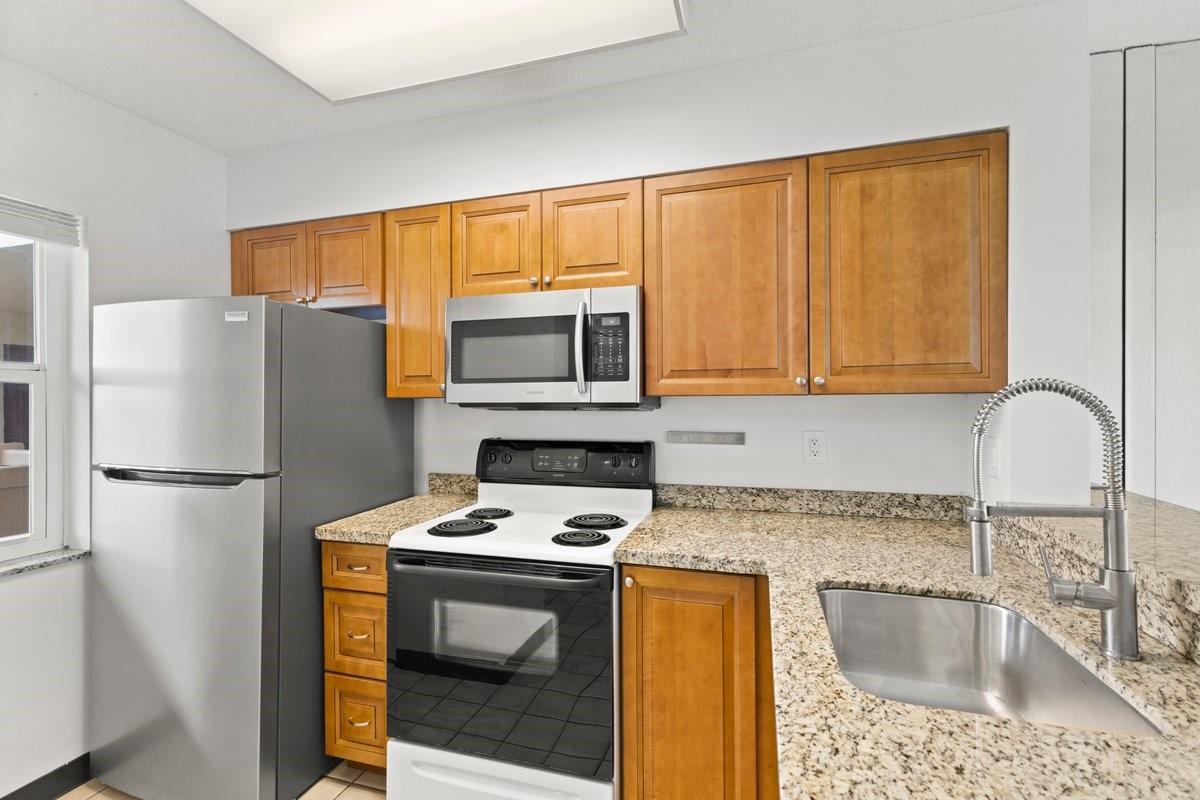 A kitchen features wood cabinets, granite countertops, a stainless steel refrigerator, and a white stove — 2106 S Cypress Bend Drive # 506, Pompano Beach FL 33069, POMPANO BEACH, FL