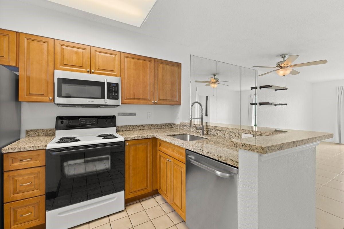 A kitchen features wood cabinets, granite countertops, stainless steel appliances, and a mirrored backsplash — 2106 S Cypress Bend Drive # 506, Pompano Beach FL 33069, POMPANO BEACH, FL