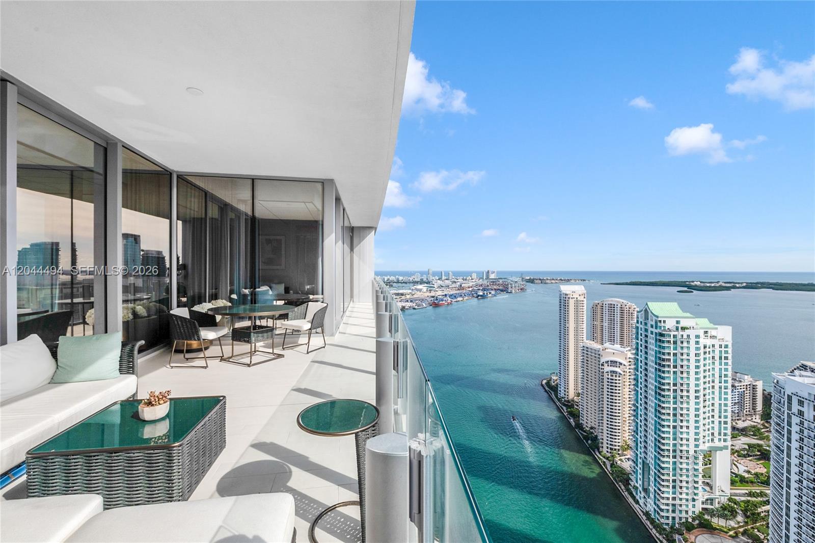 A high-rise balcony features outdoor furniture overlooking a bay, city skyline, and ocean — 300 Biscayne Blvd Way # 5104, Miami FL 33131, MIAMI, FL