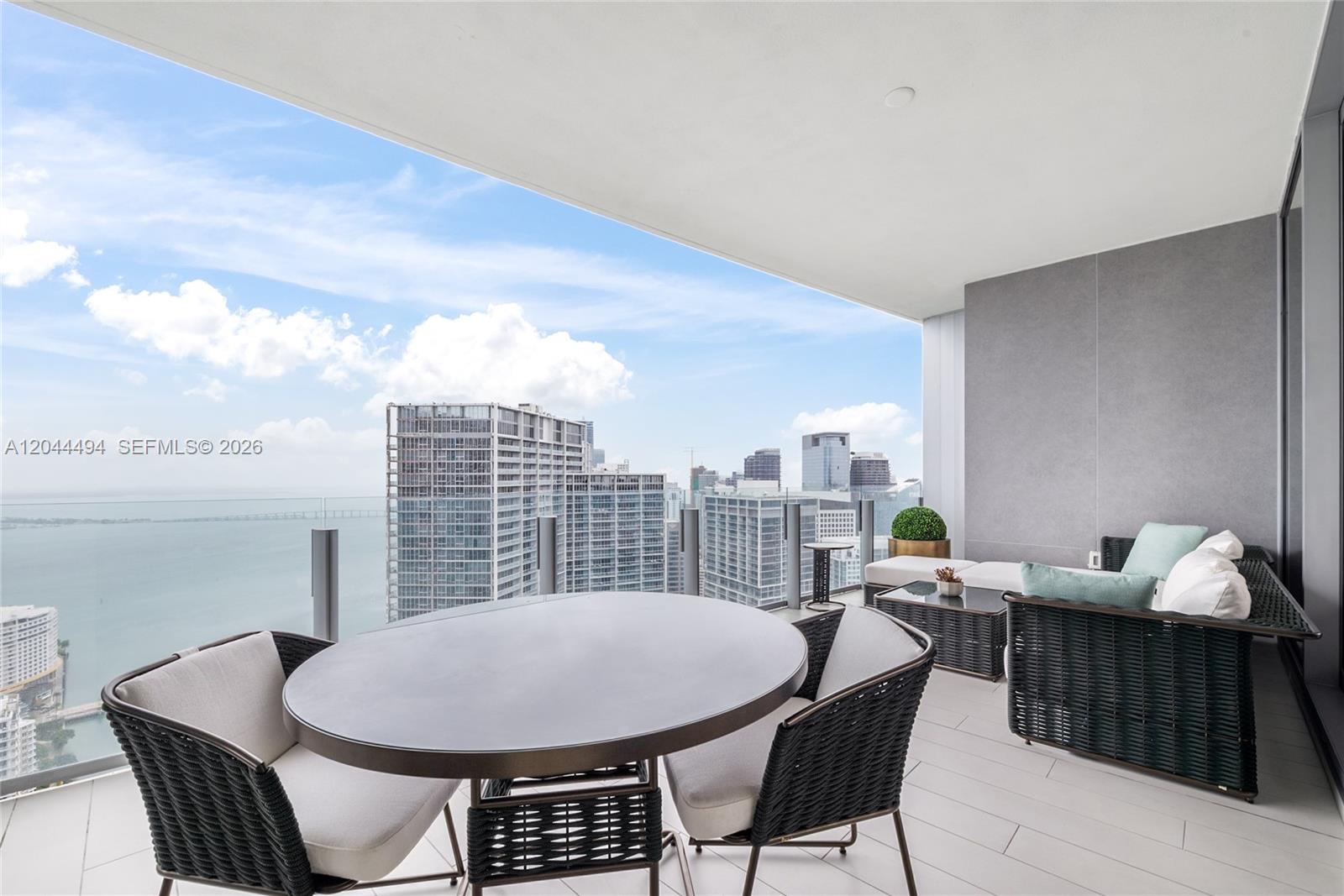 A high-rise balcony features outdoor furniture, a glass railing, and panoramic city and water views — 300 Biscayne Blvd Way # 5104, Miami FL 33131, MIAMI, FL
