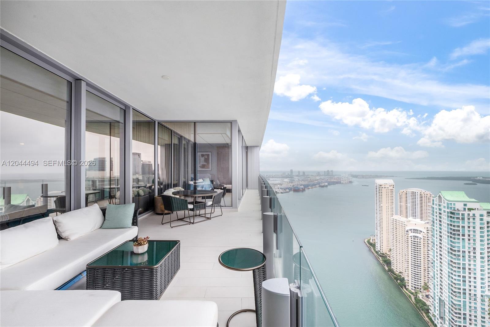 A high-rise balcony features outdoor seating and a glass railing overlooking a bay and city — 300 Biscayne Blvd Way # 5104, Miami FL 33131, MIAMI, FL