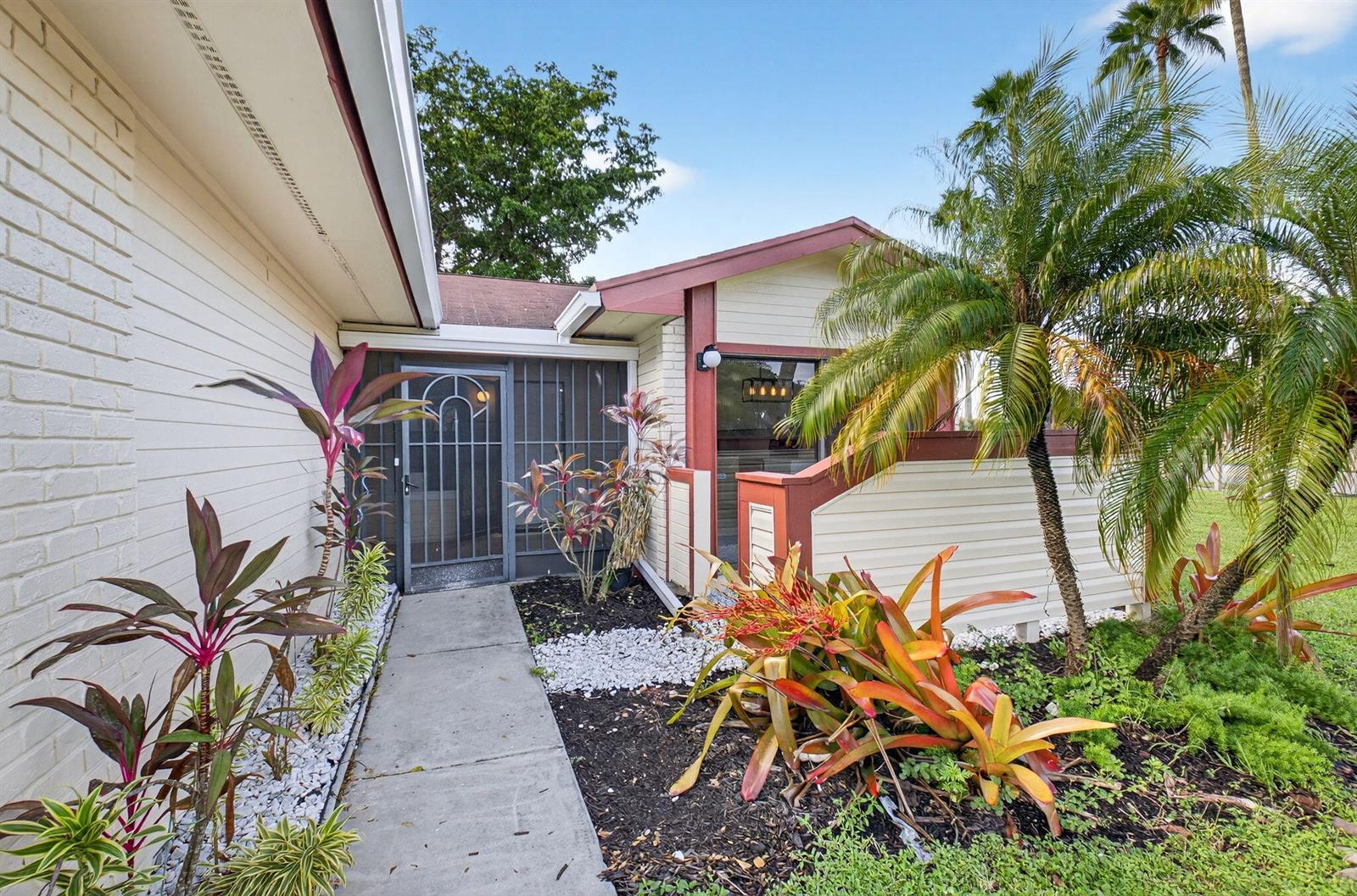 A concrete walkway leads to the screened front entrance of a house with palm trees — 29 Fawlkland Circle, Boynton Beach FL 33426, BOYNTON BEACH, FL