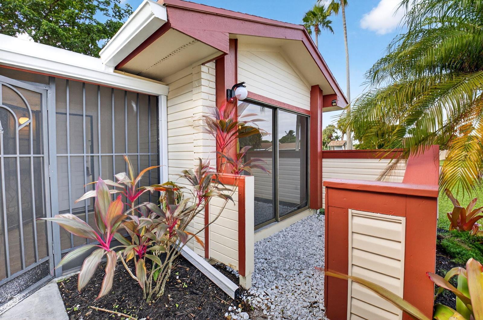 A view of a house exterior featuring a sliding glass door, gravel, and landscaping — 29 Fawlkland Circle, Boynton Beach FL 33426, BOYNTON BEACH, FL