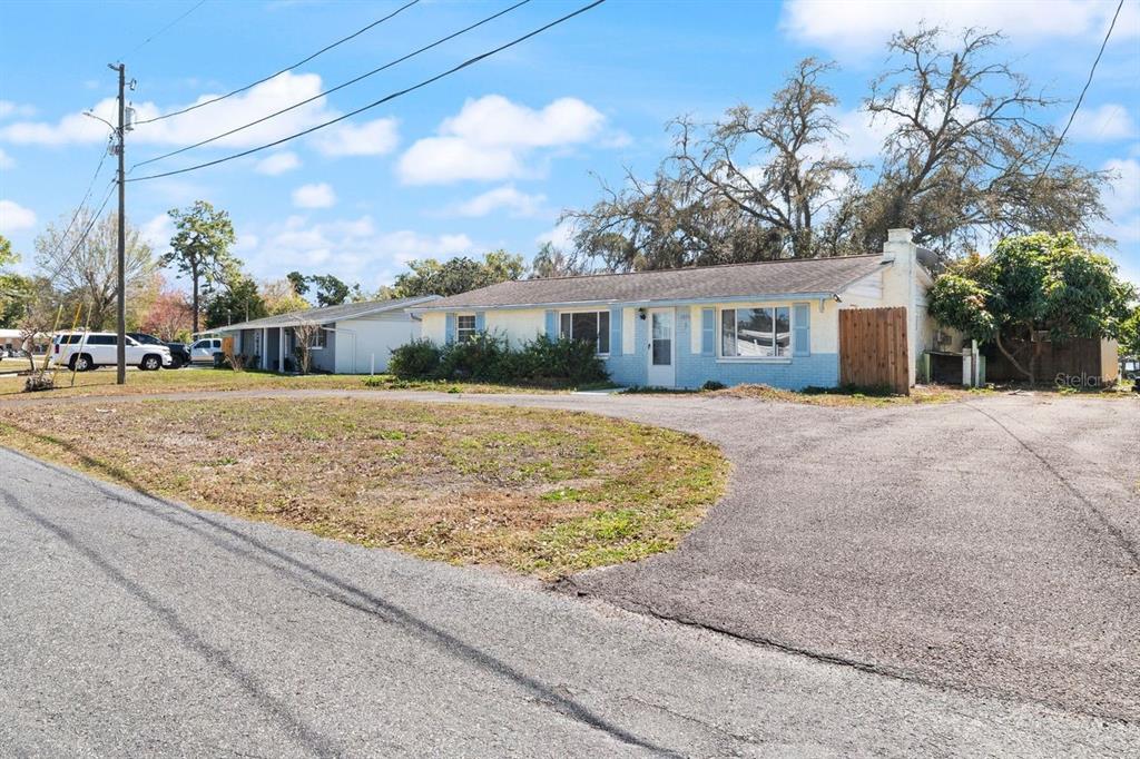 A single-story house with light blue and yellow siding sits behind a large asphalt driveway — 6870 PARKSIDE DRIVE, NEW PORT RICHEY, FL