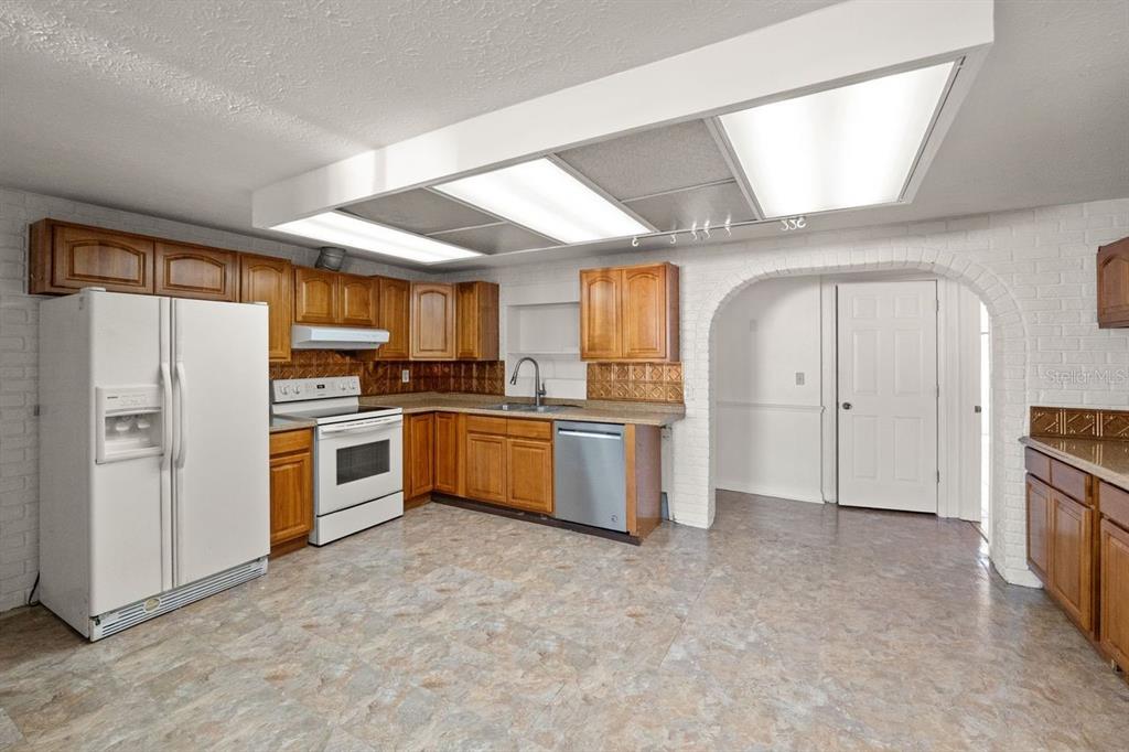 A kitchen with wood cabinets, white appliances, a tiled backsplash, and a large fluorescent light fixture — 6870 PARKSIDE DRIVE, NEW PORT RICHEY, FL