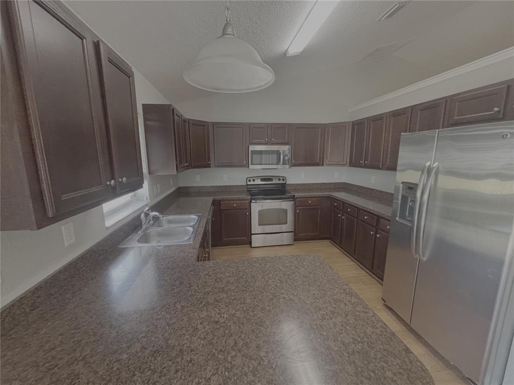 A kitchen features dark wood cabinets, brown laminate countertops, and stainless steel appliances — 9965 SW 55TH AVENUE ROAD, OCALA, FL