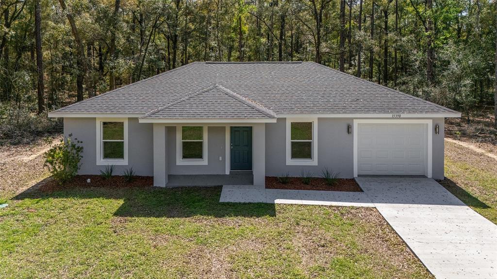 A single-story gray house with a white garage door sits in a wooded lot — 15664 SW 28TH LANE, OCALA, FL