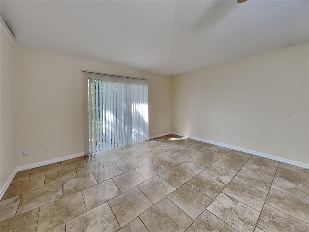 An empty room features beige walls, tile flooring, and a sliding glass door with blinds — 155 PLAIN VIEW DRIVE UNIT B, PALM COAST, FL