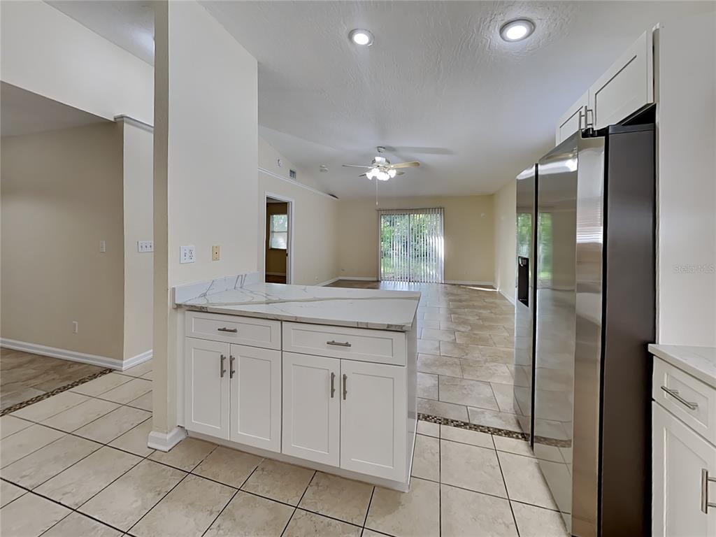A kitchen with white cabinets, marble-look countertops, and stainless steel appliances overlooks a living area — 155 PLAIN VIEW DRIVE UNIT B, PALM COAST, FL
