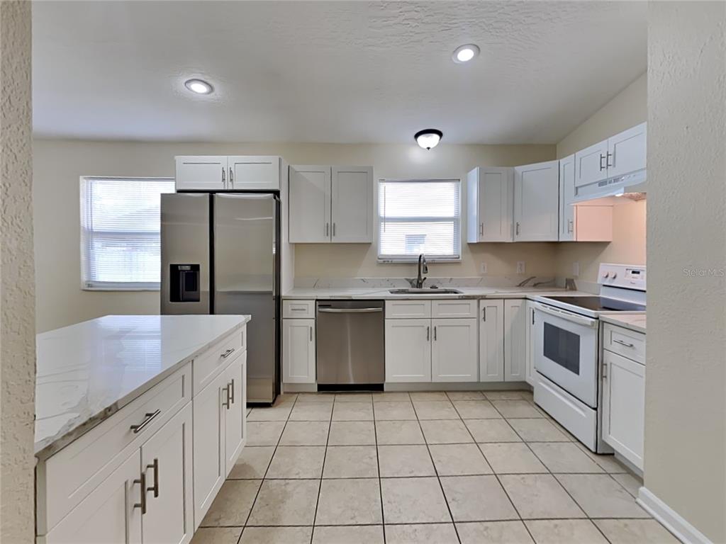 A kitchen features white cabinets, stainless steel appliances, a white island, and tiled flooring — 155 PLAIN VIEW DRIVE UNIT B, PALM COAST, FL