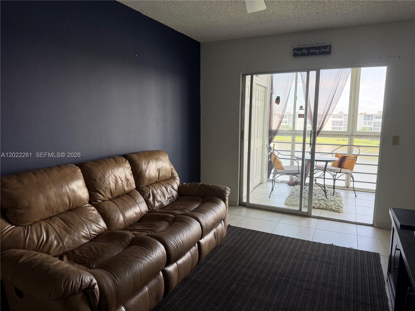 A living room features a brown leather sofa, a dark accent wall, and a sliding glass door — 4043 Cornwall C # 4043, Boca Raton FL 33434, BOCA RATON, FL