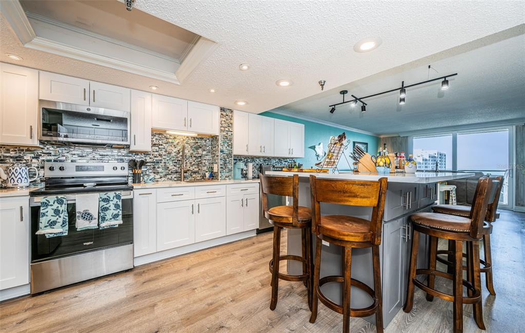 A kitchen with white cabinets, a gray island with bar stools, and a mosaic backsplash — 6035 SEA RANCH DRIVE UNIT 505, HUDSON, FL