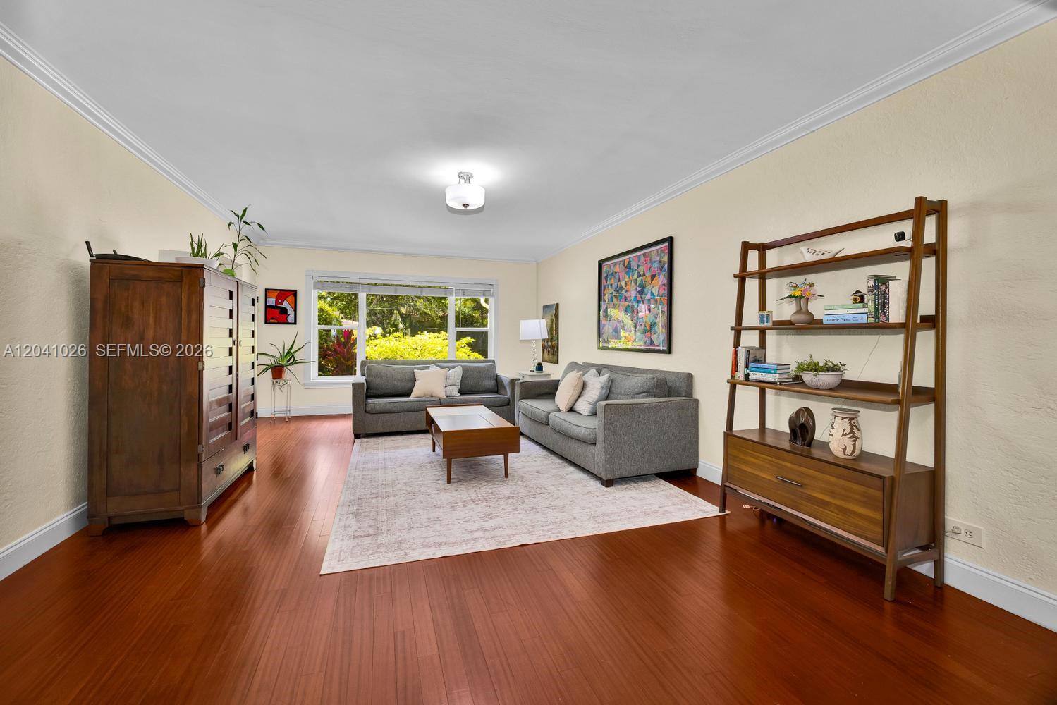 A living room features hardwood floors, two gray sofas, a coffee table, and a bookshelf — 829 Medina Ave, Coral Gables FL 33134, CORAL GABLES, FL