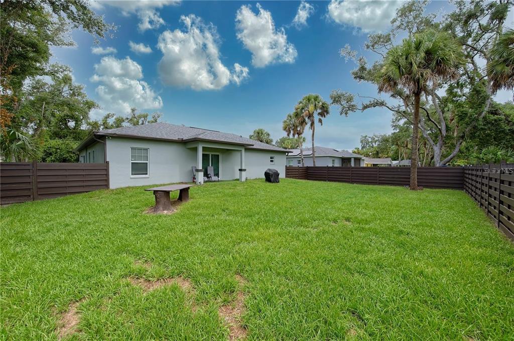 A grassy backyard features a light-colored house, a wooden bench, and dark horizontal privacy fencing — 1826 KIRKWOOD STREET, NORTH PORT, FL