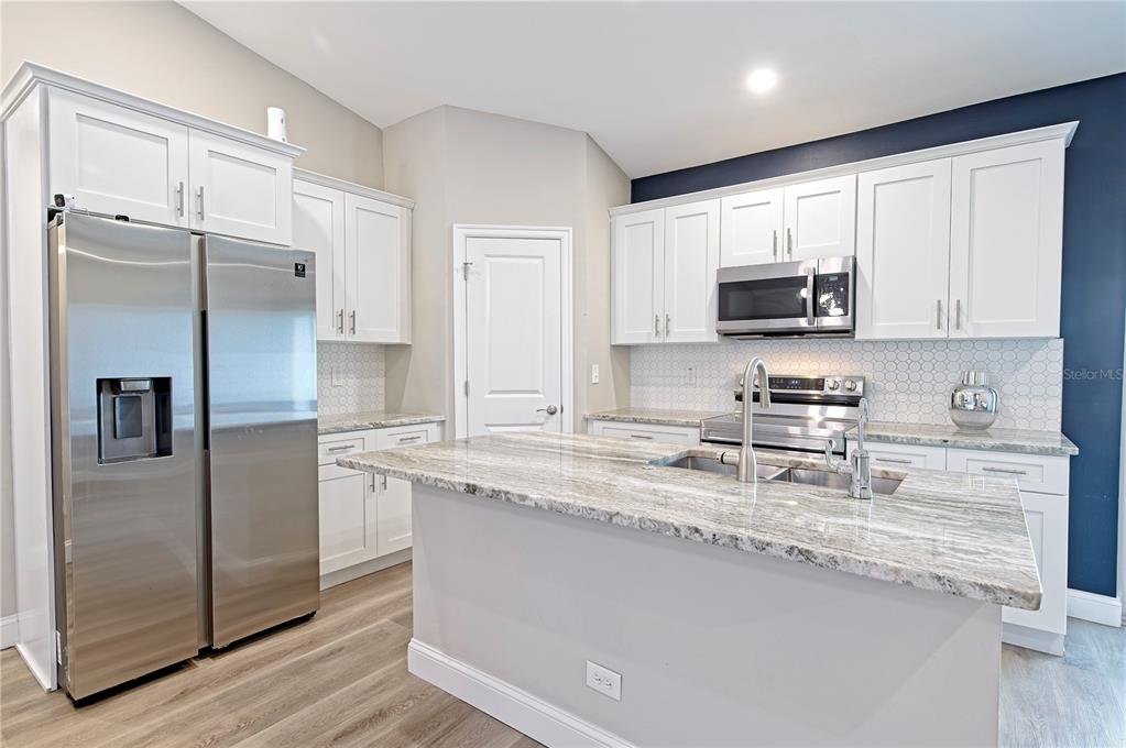 A kitchen features white cabinets, stainless steel appliances, a granite island, and light wood flooring — 1826 KIRKWOOD STREET, NORTH PORT, FL