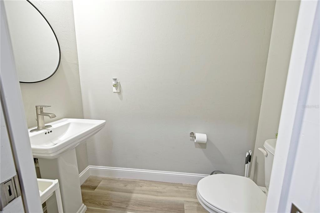 A small bathroom features a pedestal sink, a round mirror, and a white toilet — 1826 KIRKWOOD STREET, NORTH PORT, FL