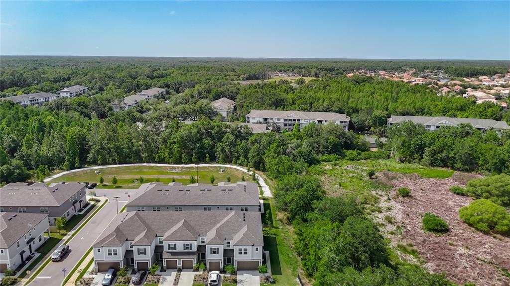An aerial view shows multi-story townhomes surrounded by dense trees and undeveloped land — 10801 FORT WHITE COURT, TAMPA, FL