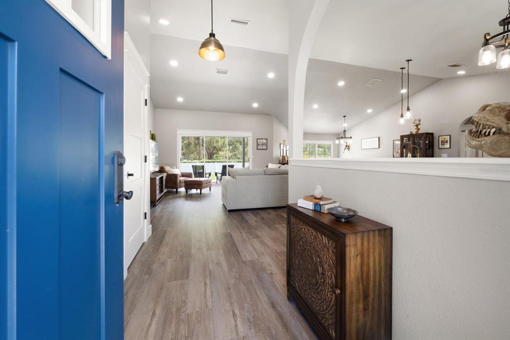 A view from a blue front door into an open-concept living area with wood flooring — 668 MEHLENBACHER ROAD, BELLEAIR, FL