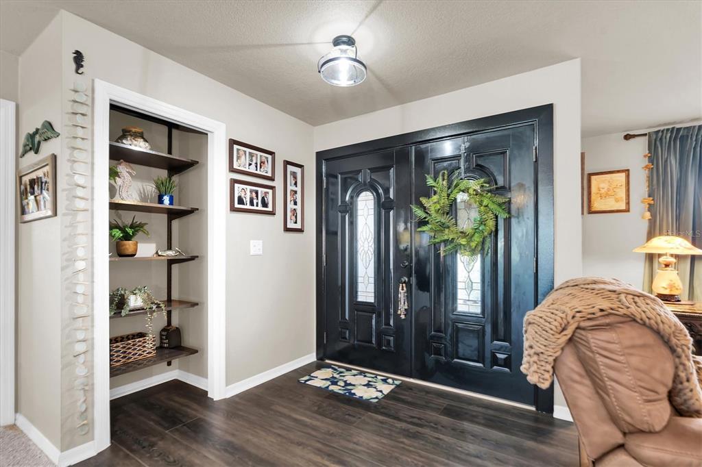 An entryway features dark double doors, wood-look flooring, and a built-in shelving unit — 301 THORN HILL PLACE, SUN CITY CENTER, FL