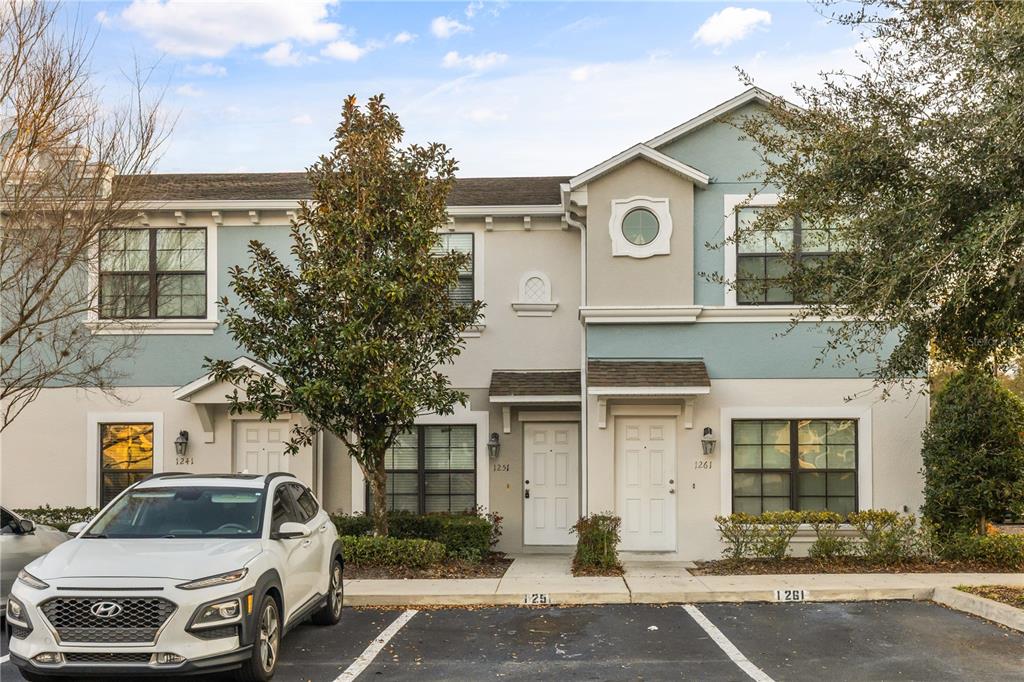 A two-story townhouse exterior features light blue and beige siding with a white car parked — 1251 TRILLIUM PARK LANE, SANFORD, FL