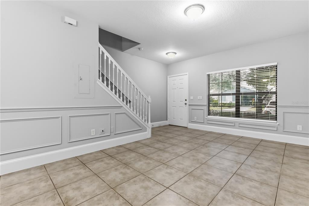 An empty room with tiled floors, white wainscoting, a staircase, and a front entrance door — 1251 TRILLIUM PARK LANE, SANFORD, FL