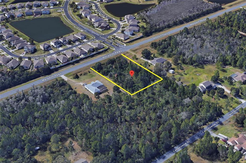 An aerial view shows a vacant, wooded lot outlined in yellow along a paved road — 0 MEREDITH PARKWAY, ORLANDO, FL