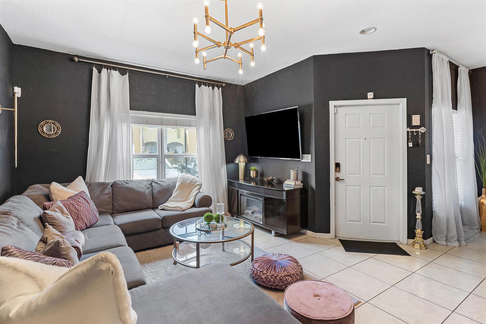 A living room features dark walls, a grey sectional sofa, and a modern gold chandelier — 2851 W Prospect # 506, Tamarac FL 33309, TAMARAC, FL