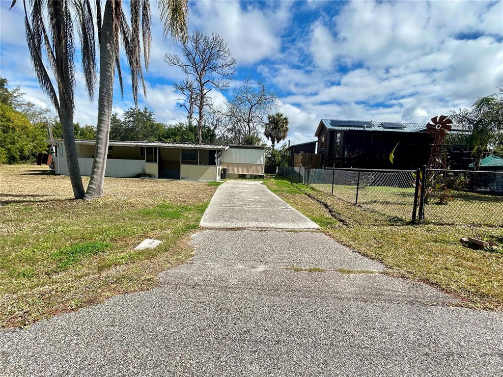 A concrete driveway leads to a single-story house with a screened porch and palm trees — 6116 COUNTRYMAN LANE, NEW PORT RICHEY, FL