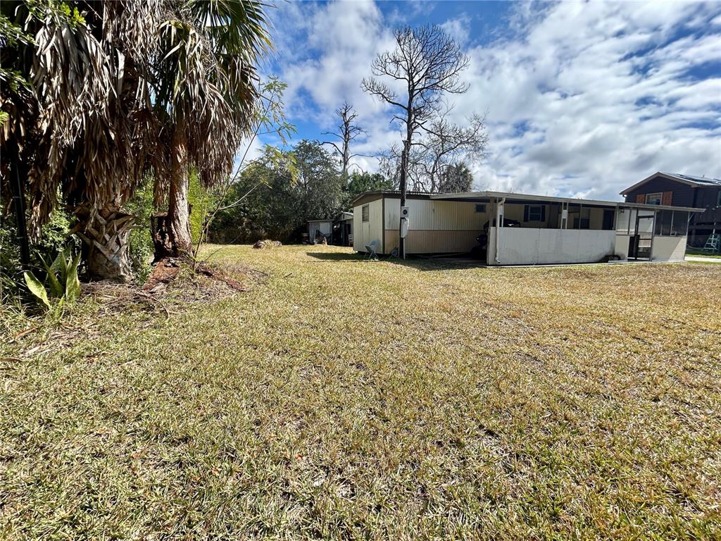 A mobile home with a carport sits on a grassy lot near some trees — 6116 COUNTRYMAN LANE, NEW PORT RICHEY, FL