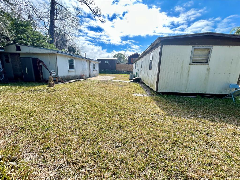 A grassy backyard area sits between two single-story residential structures under a cloudy sky — 6116 COUNTRYMAN LANE, NEW PORT RICHEY, FL