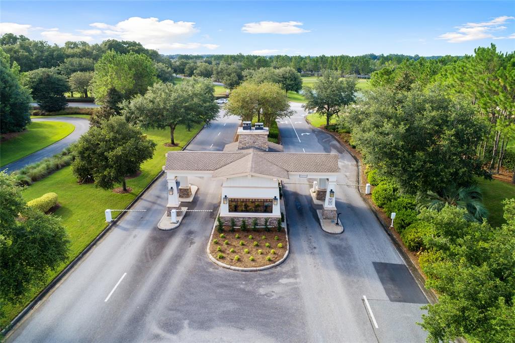 An aerial view of a gated community entrance with a stone and stucco guardhouse — 6606 SW 91ST CIRCLE UNIT 6606, OCALA, FL