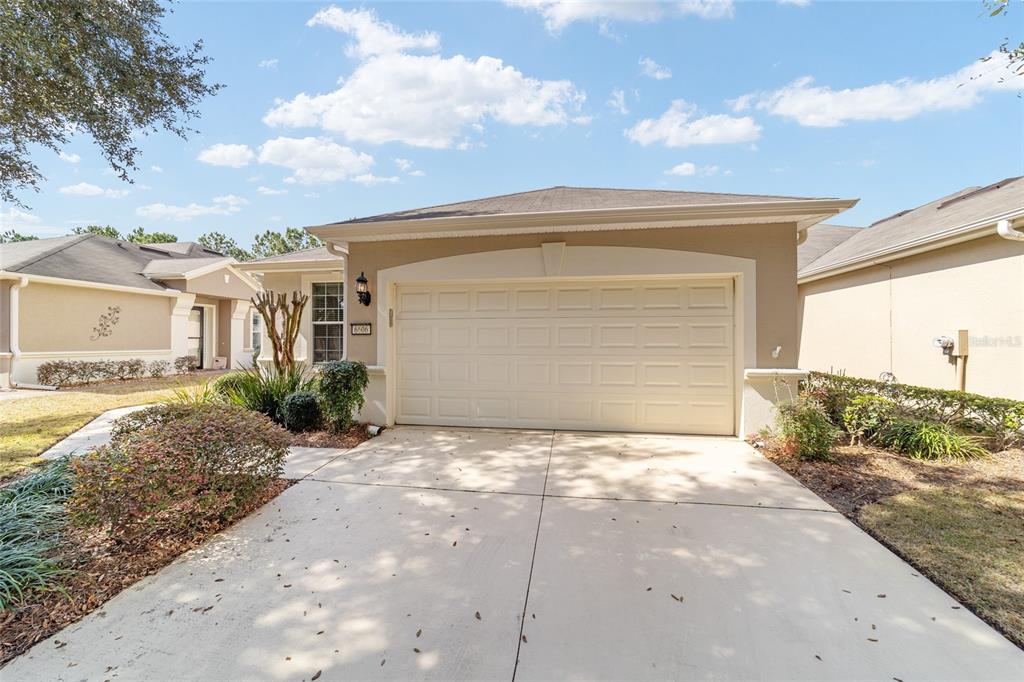 A beige house exterior features a two-car garage, a concrete driveway, and landscaped front yard — 6606 SW 91ST CIRCLE UNIT 6606, OCALA, FL