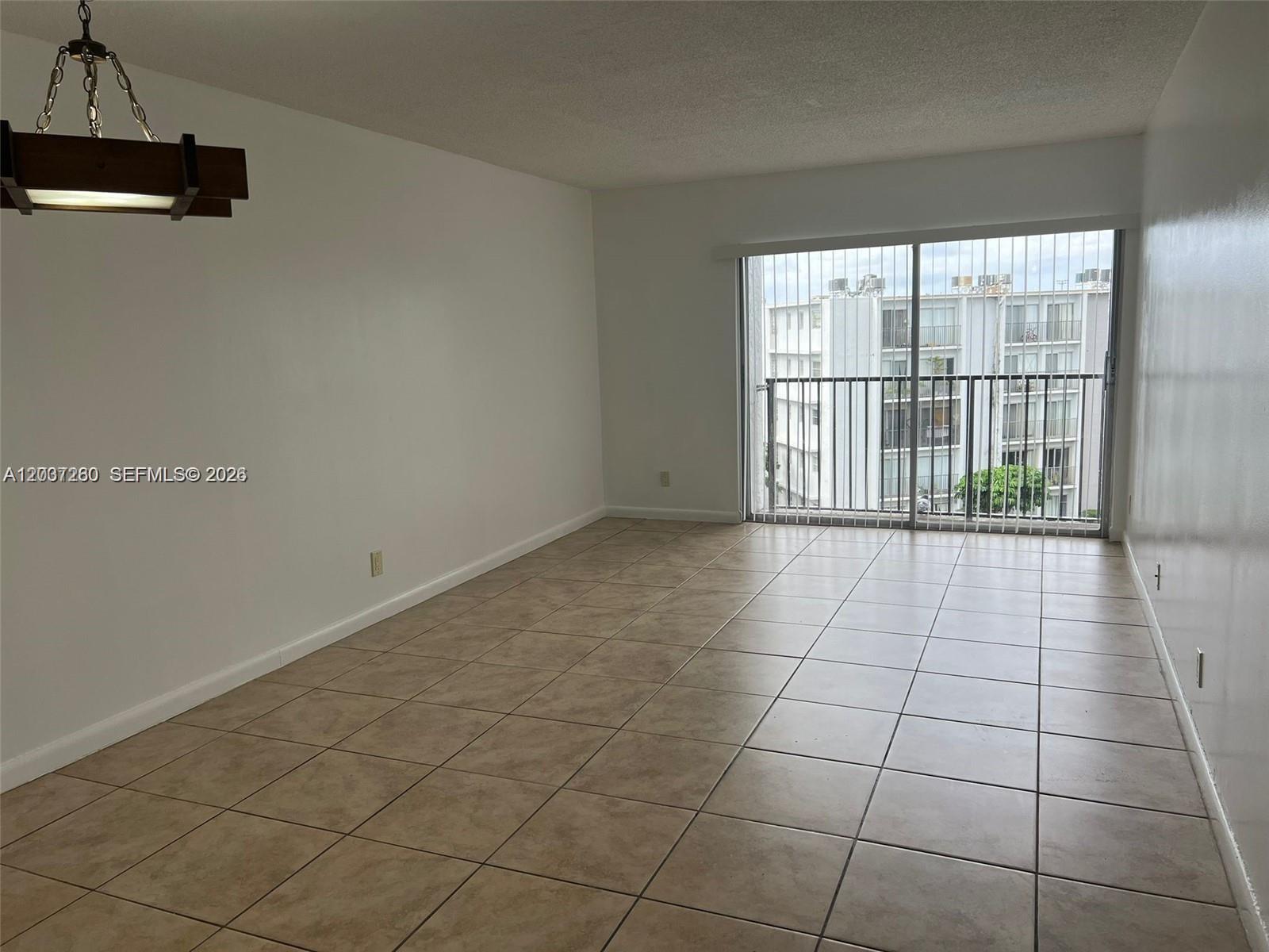 An empty room features beige tile flooring, white walls, a hanging light fixture, and a balcony — 8610 N Sherman Cir # 504, Miramar FL 33025, MIRAMAR, FL
