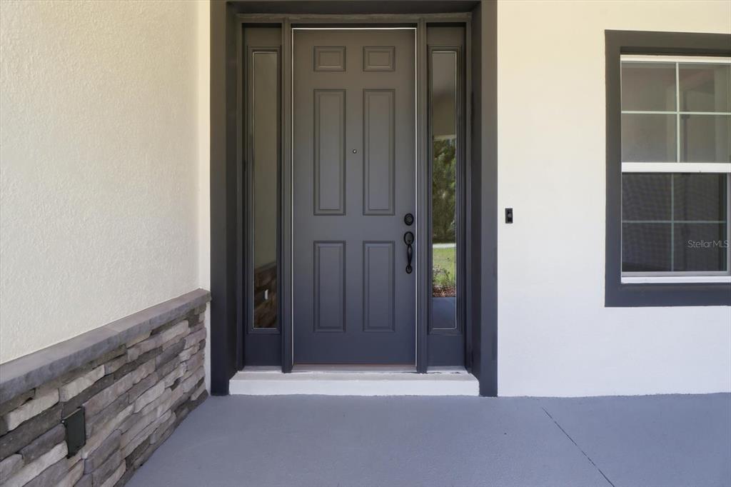 A dark gray front door with sidelights is set against a white wall with stone accents — 3880 SW 131ST PLACE RD, OCALA, FL