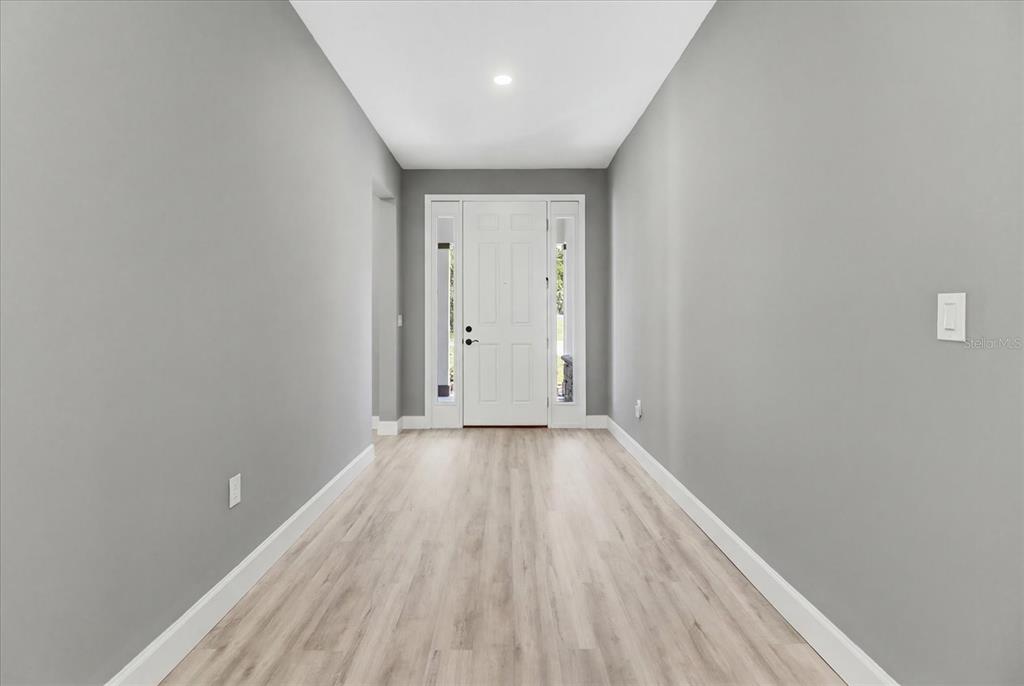 A bright entryway features light wood-look flooring, gray walls, and a white front door — 3880 SW 131ST PLACE RD, OCALA, FL