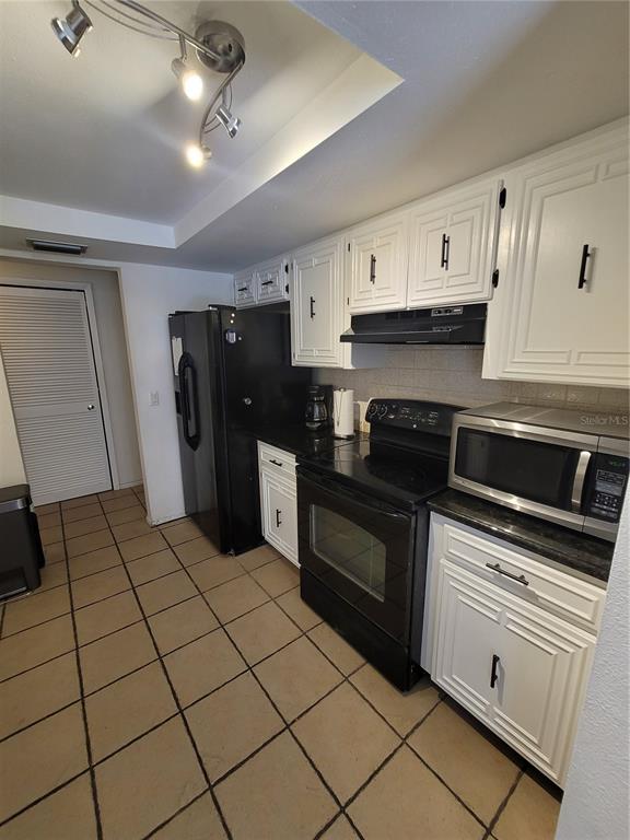 A kitchen features white cabinets, black appliances, dark countertops, and tan tile flooring — 9826 LEHIGH DRIVE, PORT RICHEY, FL