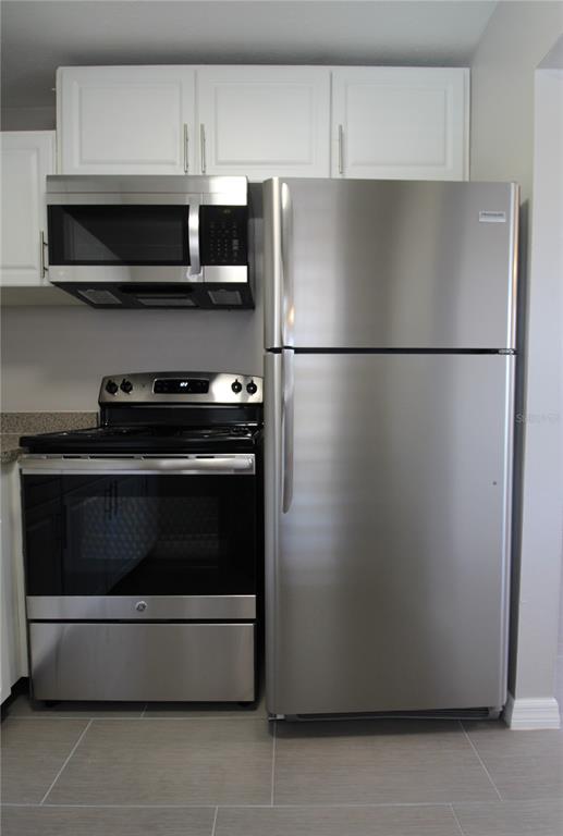 A kitchen features stainless steel appliances, white cabinets, and gray tile flooring — 3001 BEE RIDGE ROAD UNIT 224, SARASOTA, FL