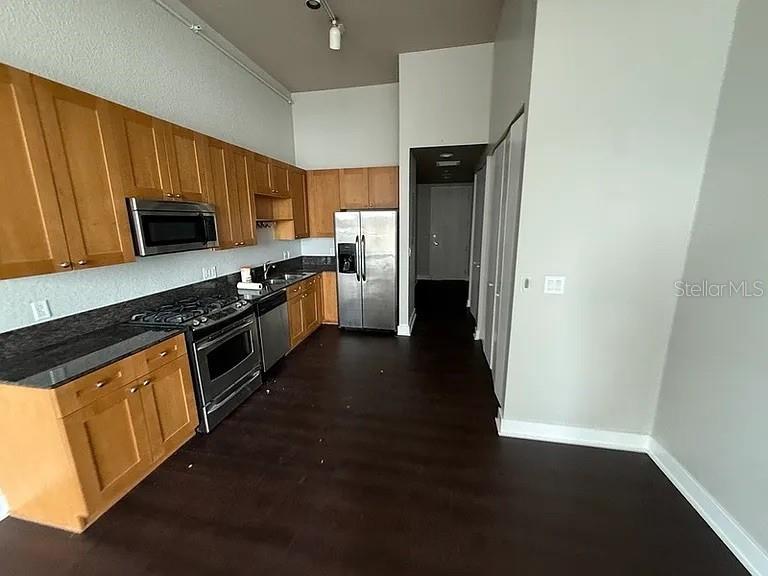 A kitchen features light wood cabinets, stainless steel appliances, dark countertops, and dark wood flooring — 150 E ROBINSON STREET UNIT 627, ORLANDO, FL