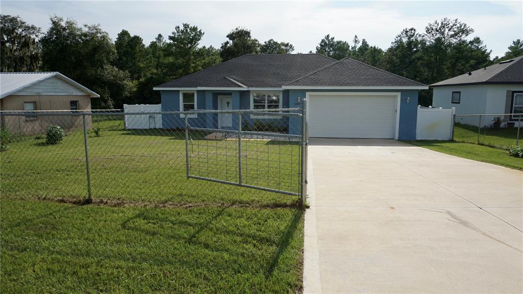A blue single-story house with a two-car garage and a chain-link fence in front — 32831 FOREST AVENUE, LEESBURG, FL
