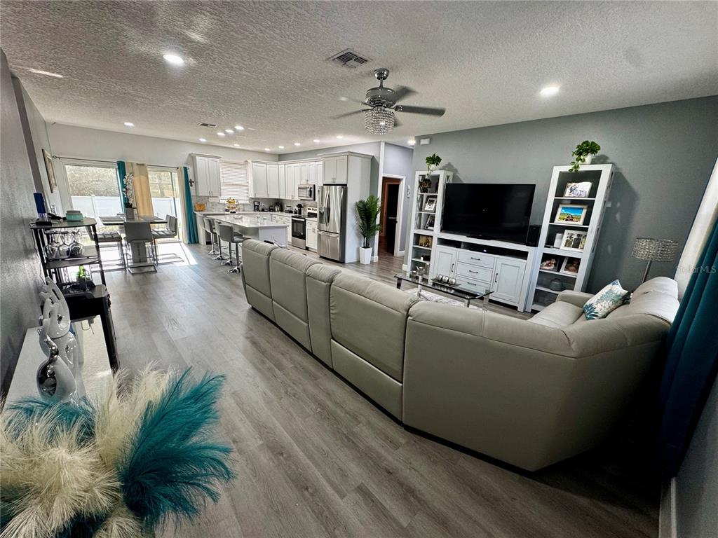 An open-concept living room and kitchen featuring light wood flooring and white cabinetry — 32831 FOREST AVENUE, LEESBURG, FL