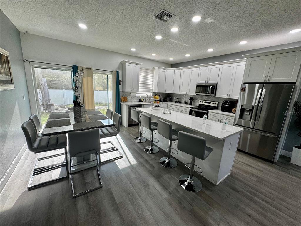 A modern kitchen features white cabinetry, a large island with bar stools, and dining area — 32831 FOREST AVENUE, LEESBURG, FL