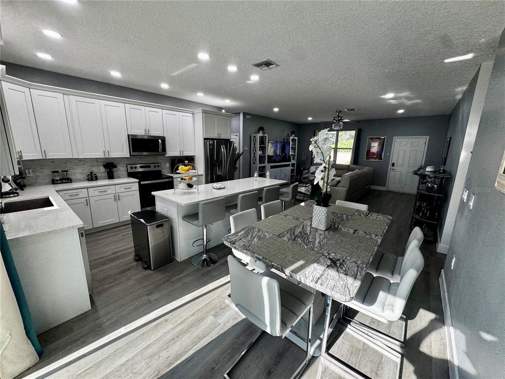 An open-concept kitchen and dining area featuring white cabinets, a kitchen island, and gray flooring — 32831 FOREST AVENUE, LEESBURG, FL