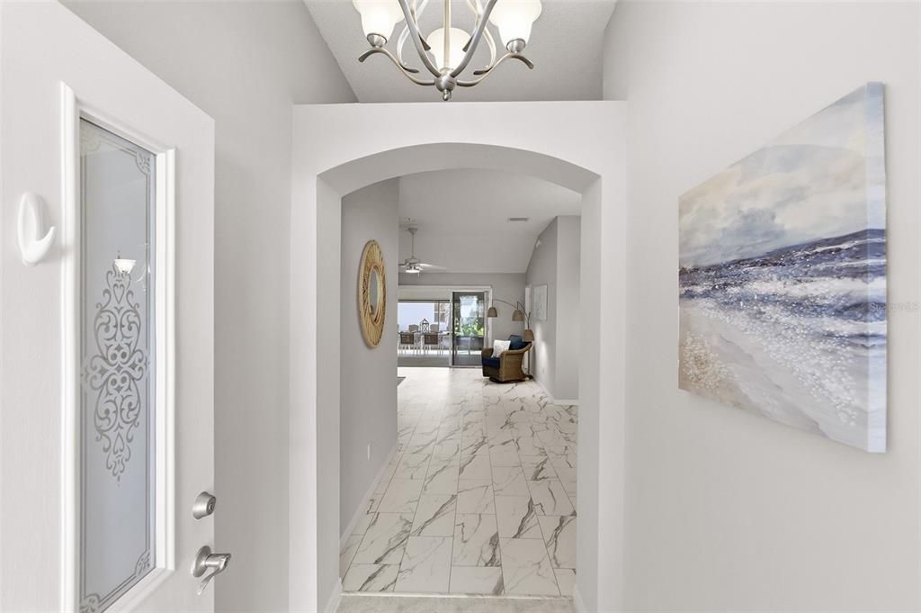 An entryway with white marble-look tile flooring leads through an arched doorway into a living area — 2261 WELCOME WAY, THE VILLAGES, FL