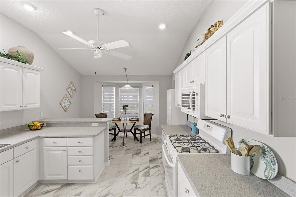 A white kitchen features marble-look tile floors, white cabinetry, and an adjacent dining nook — 2261 WELCOME WAY, THE VILLAGES, FL