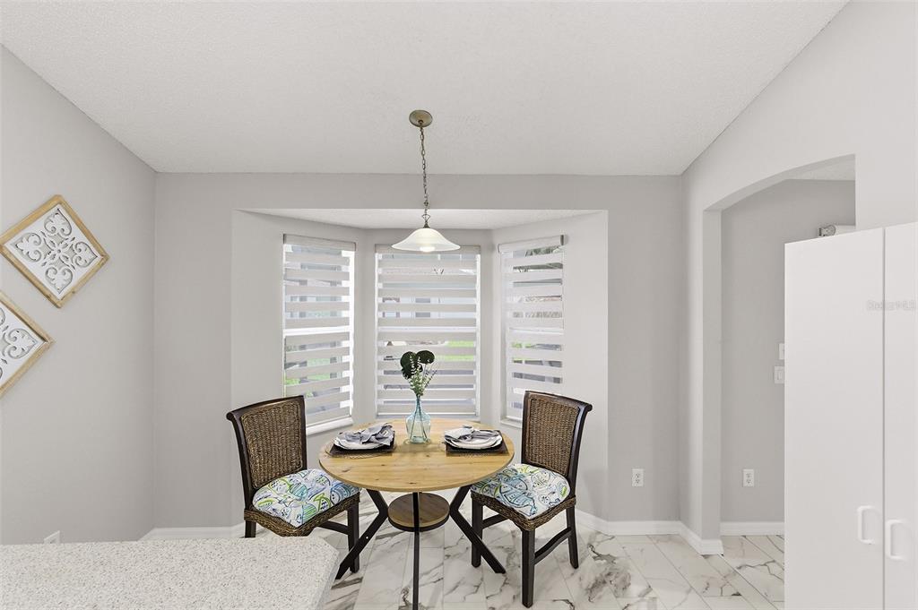A dining nook features a round wooden table, two wicker chairs, and a bay window — 2261 WELCOME WAY, THE VILLAGES, FL