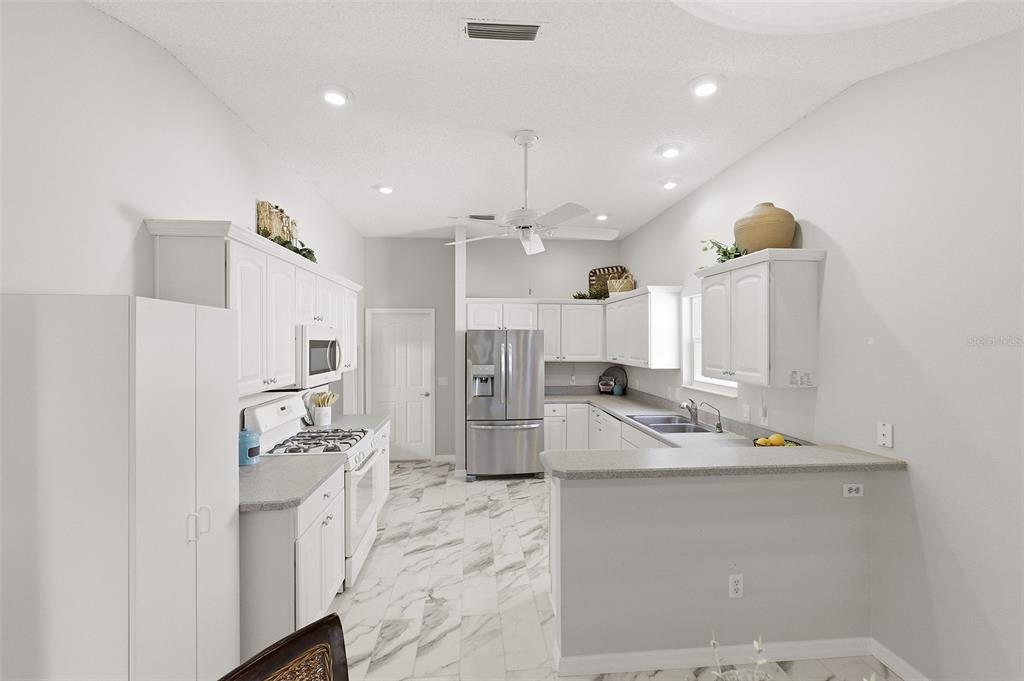 A white kitchen features stainless steel appliances, marble-patterned tile floors, and a breakfast bar — 2261 WELCOME WAY, THE VILLAGES, FL